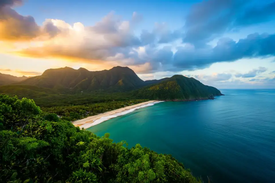 Vue panoramique de la côte brésilienne avec montagnes verdoyantes plongeant dans l'océan turquoise, lumière dorée de fin de journée
