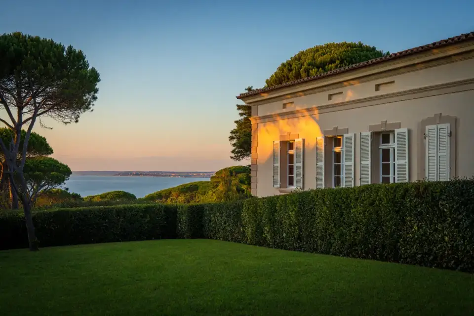 Villa néo-XIXe au Cap-Ferret, façade crème entourée de pins maritimes, lumière dorée du soir, bassin d'Arcachon en arrière-plan