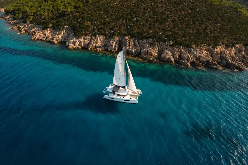 Catamaran blanc naviguant le long de la côte corse, eau turquoise et falaises de granit en arrière-plan