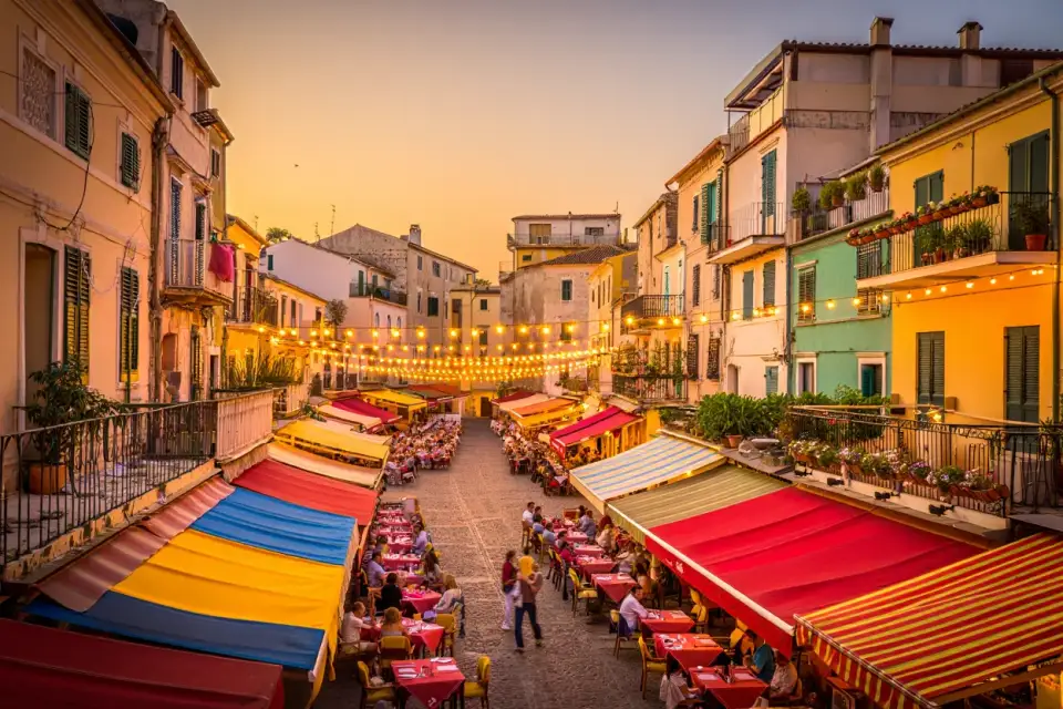 Terrasses de restaurants animées sur une place européenne au coucher du soleil, architecture méditerranéenne colorée, lumière dorée, pavés, voyageurs attablés
