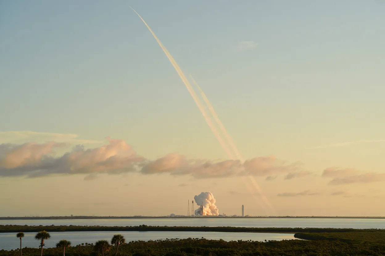 Paysage de la Space Coast en Floride avec traînée de fusée traversant un ciel bleu pâle au-dessus du Kennedy Space Center