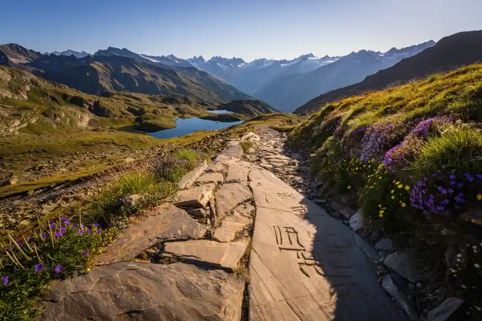 Sentier de randonnée dans le Mercantour, dalles de schiste polies avec lacs glaciaires et sommets alpins en arrière-plan