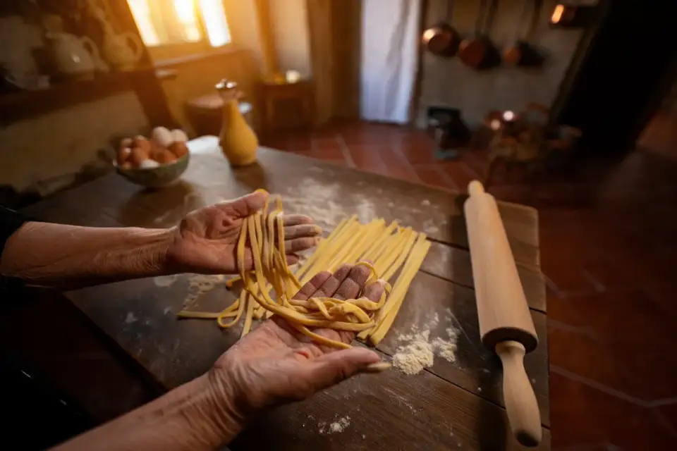 Mains d'une grand-mère italienne façonnant des pâtes fraîches sur une table en bois à Rome, lumière dorée, farine et œufs, cuisine méditerranéenne authentique