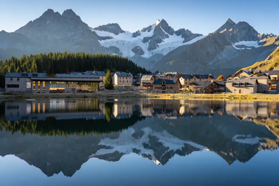 Village de Loudenvielle dans les Hautes-Pyrénées avec son lac artificiel entouré de montagnes enneigées, lumière dorée de fin de journée
