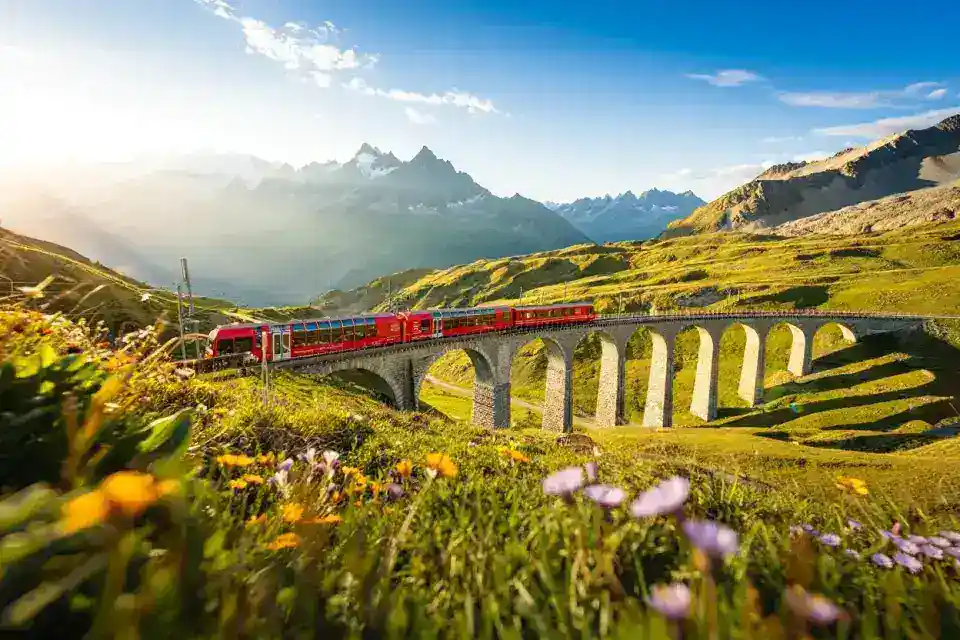 Train panoramique du Mont-Blanc Express traversant un viaduc de pierre dans les Alpes suisses, sommets enneigés et vallée verdoyante en arrière-plan