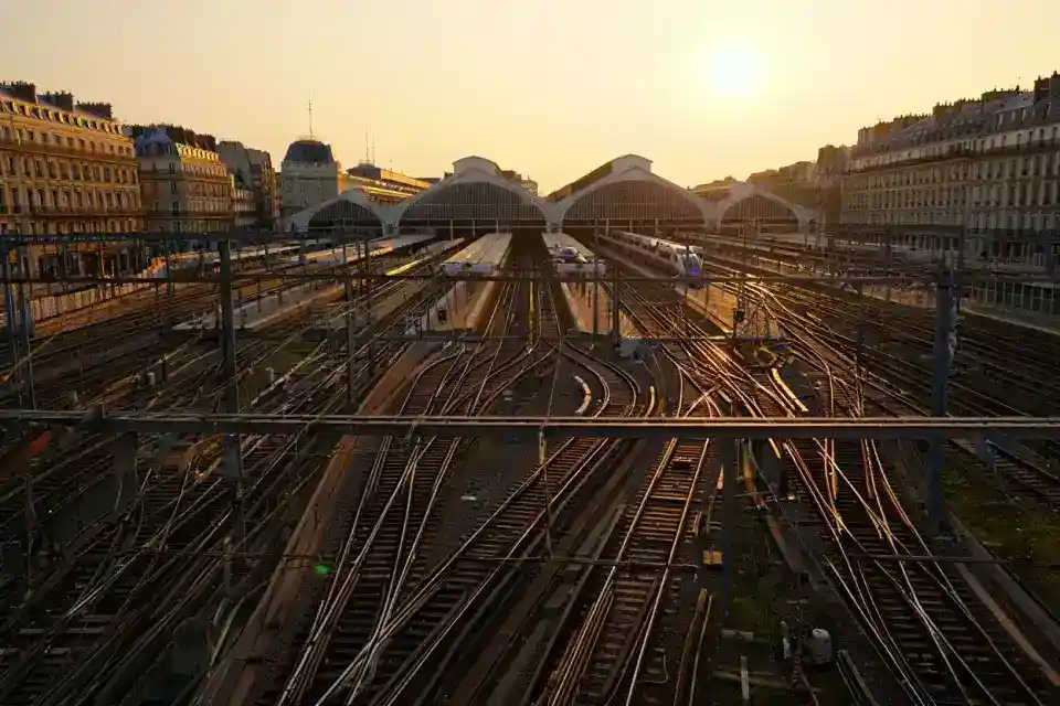 Vue aérienne des voies ferrées et aiguillages de Paris Gare de Lyon au lever du soleil, réseau complexe de rails convergents, trains TGV sur les quais, architecture parisienne en arrière-plan