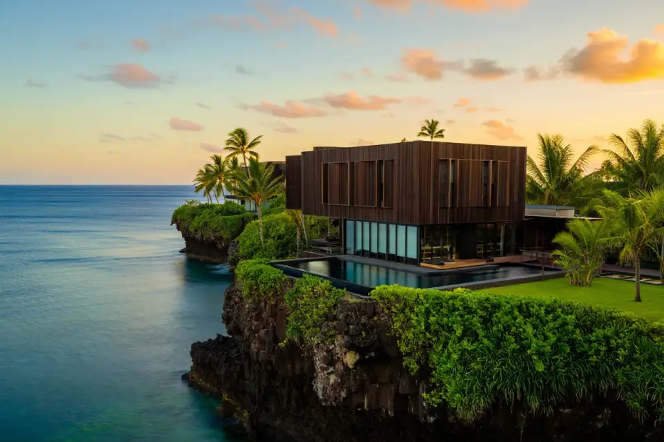 Architecture contemporaine en bois brûlé sur la côte basaltique de Trois-Bassins à La Réunion, piscine à débordement face à l'océan Indien, végétation tropicale, lumière dorée