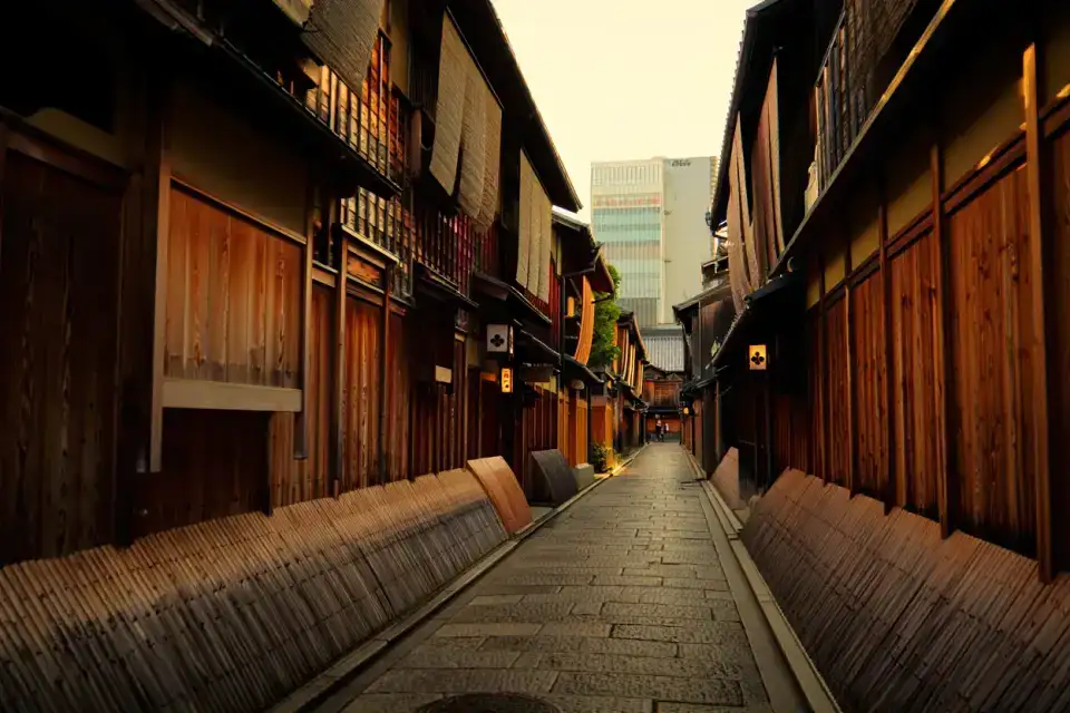 Ruelle traditionnelle de Kagurazaka à Tokyo, façades en bois à claire-voie, lanternes en pierre et lumière dorée du matin avec un gratte-ciel moderne en arrière-plan
