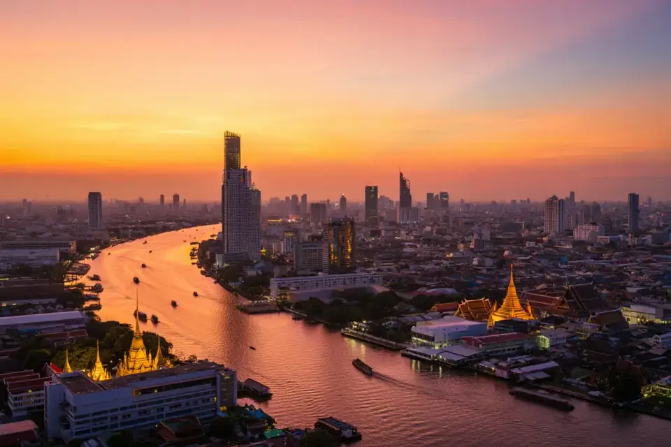 Vue panoramique d'une ville côtière asiatique au coucher du soleil avec temples et gratte-ciels, bateaux dans le port et lumière dorée