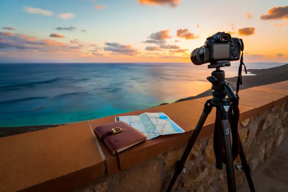Appareil photo et carnet de voyage posés sur un muret de pierre dominant une côte méditerranéenne au coucher du soleil