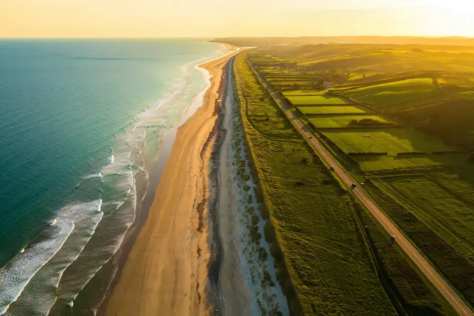 Route côtière de Bretagne au coucher du soleil, falaises et mer turquoise, voiture solitaire sur la route, ciel doré, atmosphère estivale paisible